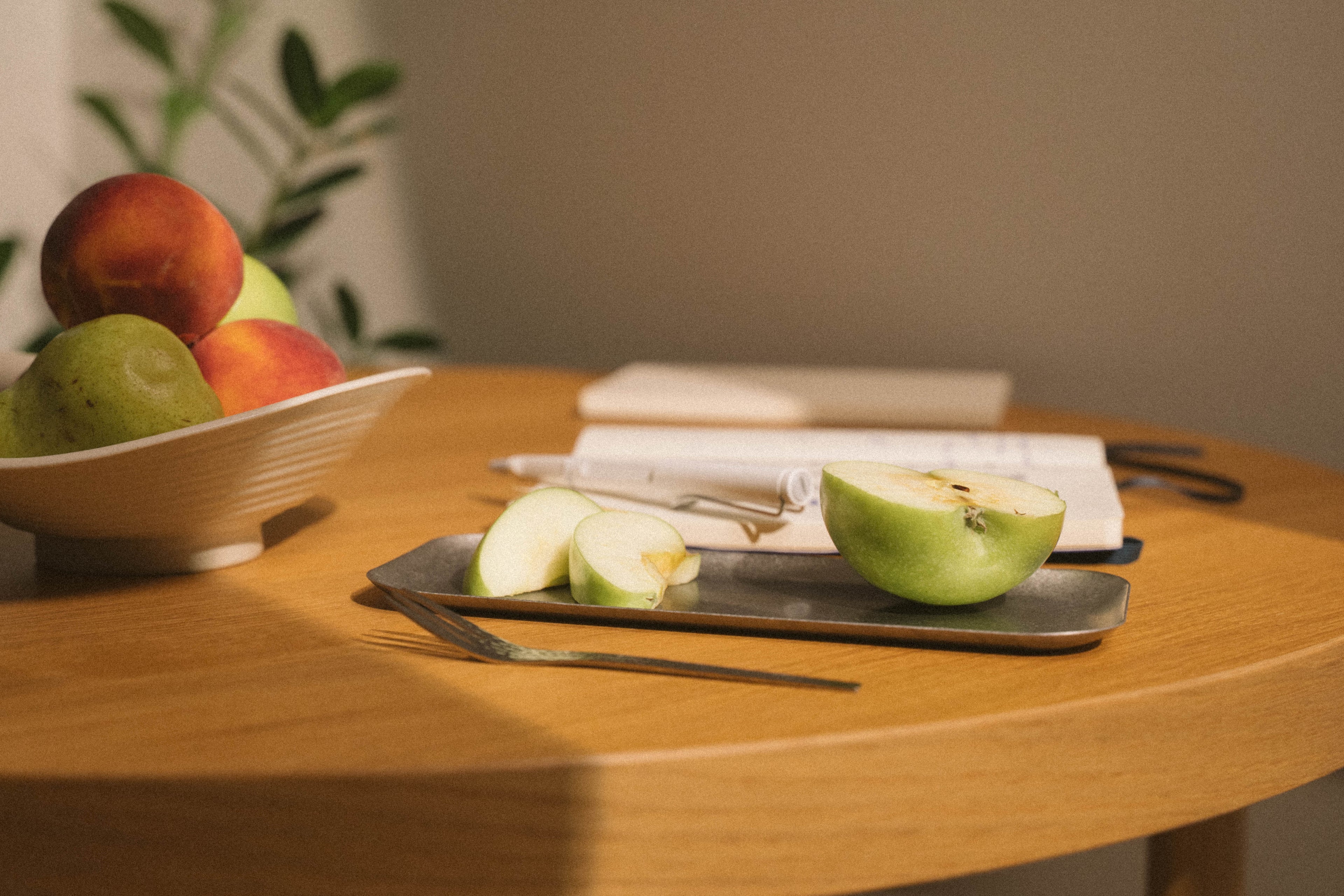 Apples on a table with a bowl and books in the background
